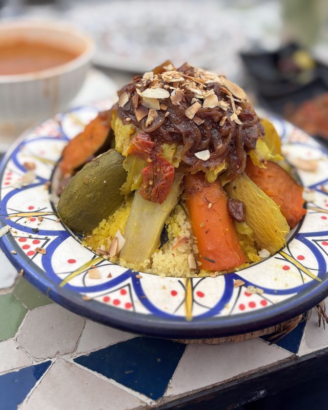 Couscous aux légumes couronné de tfaya et d'amandes, servi sur table en zellige