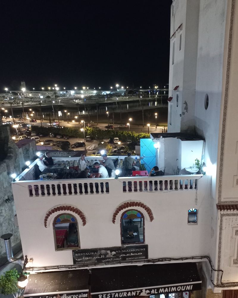 La maison à la nuit tombée — terrasse pleine au-dessus de l'enseigne, le boulevard du port derrière